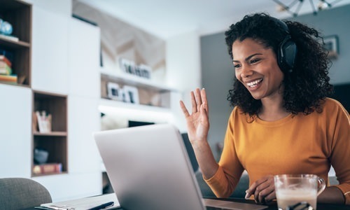 woman with headphones waving at her laptop